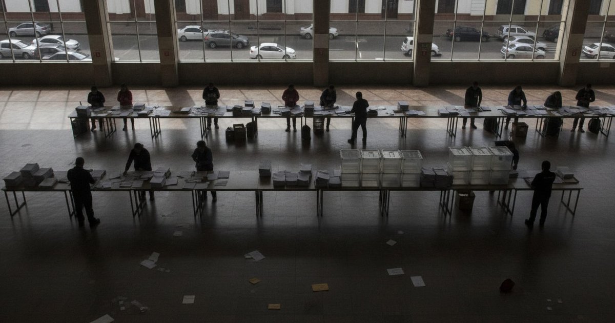 Voluntarios organizan mesas y urnas en un centro de votación de América Latina, con papeleo y documentos electorales.