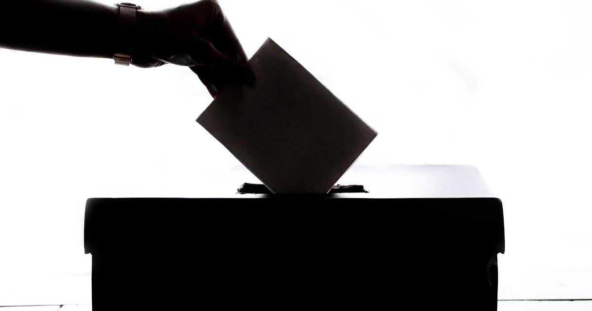 Silueta de una mano introduciendo un sobre de votación en una urna