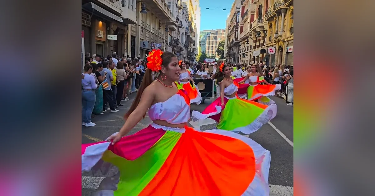 Participantes con coloridos trajes folclóricos hispanoamericanos desfilan por la Plaza de la Reina en Valencia durante la celebración del Día de la Hispanidad.